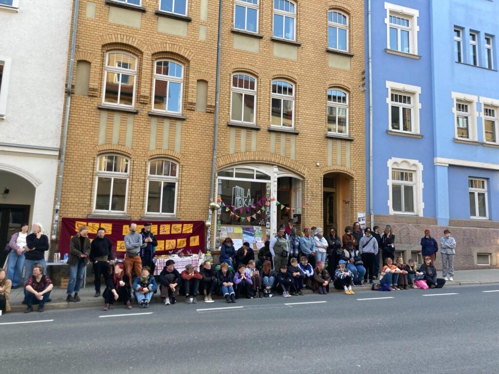 große Menge an Menschen steht und sitzt vor dem Lila Lokal